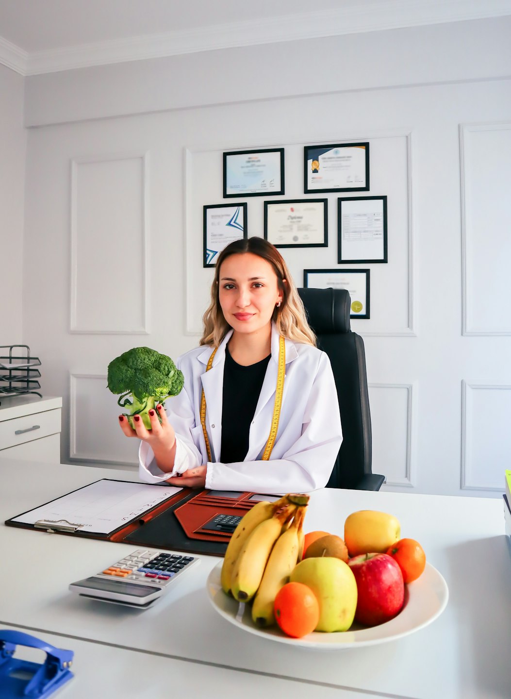 Dietitian holds broccoli and smiles at a desk.