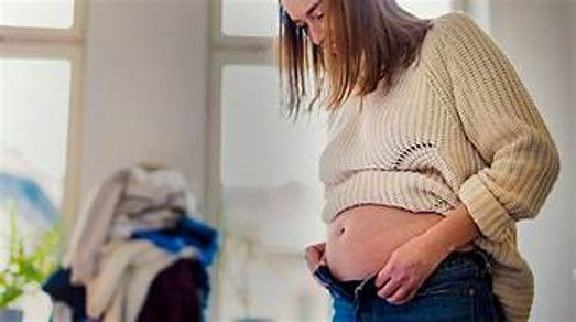 woman having trouble buttoning her pants because of belly fat and the over hang of fat.
